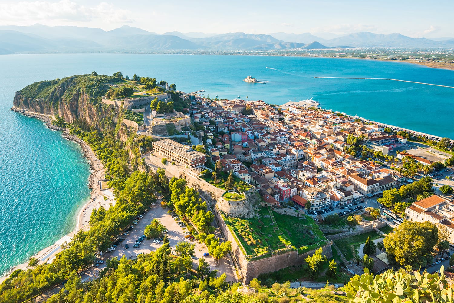Πράσινη χερσόνησος με την πόλη του Ναυπλίου στην Ελλάδα από ψηλά με τη γαλάζια θάλασσα της Μεσογείου, τις στέγες της παλιάς πόλης και το μικρό λιμάνι
