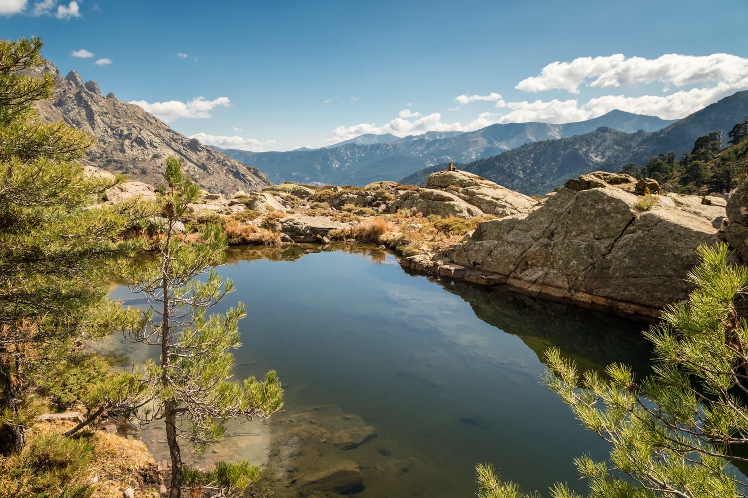 Small lake at Paglia Orba surrounded by rocks, pine trees and mountains near the GR20 hiking trail in central Corsica