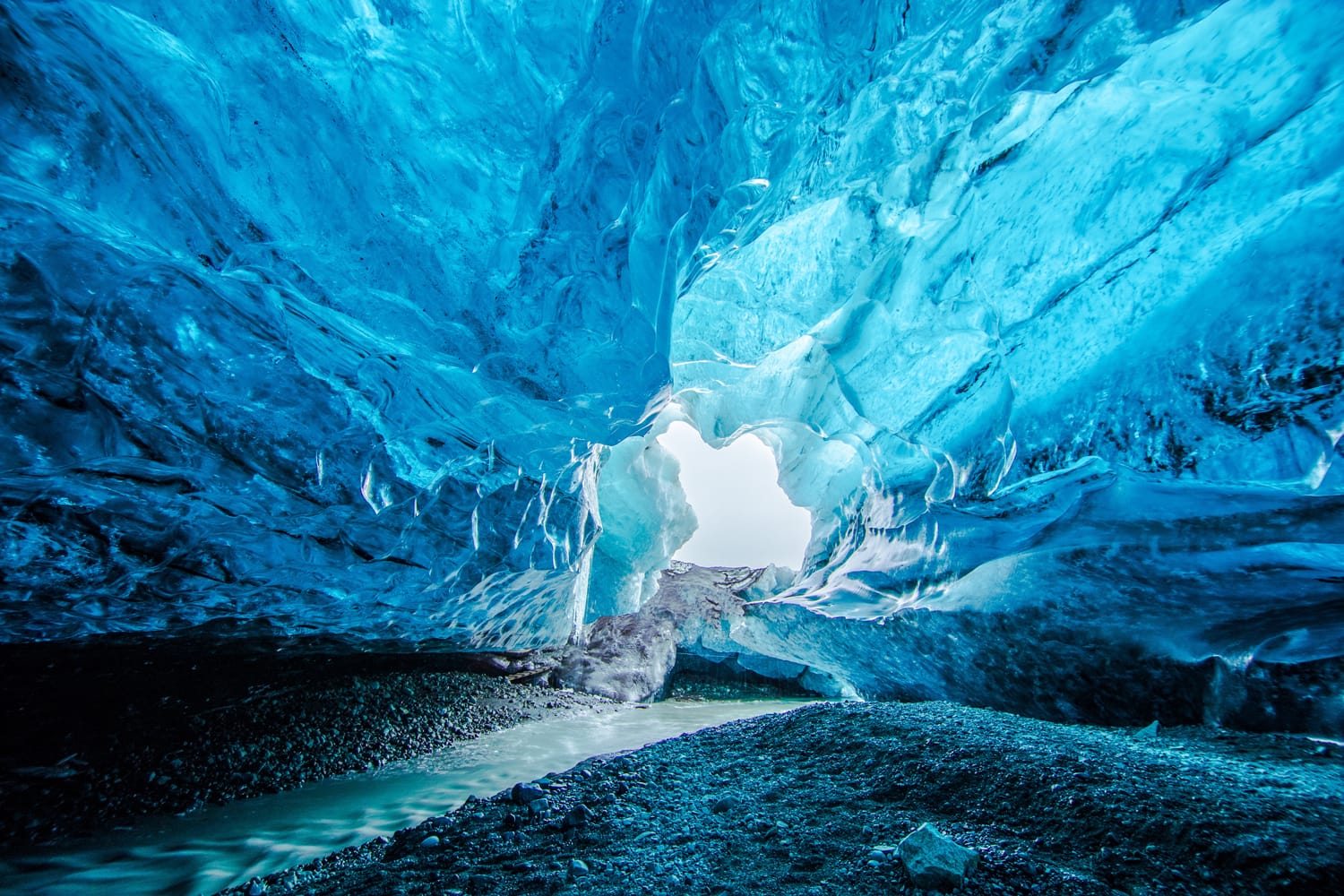 Blue crystal ice cave entrance and an underground river beneath the glacier in Iceland