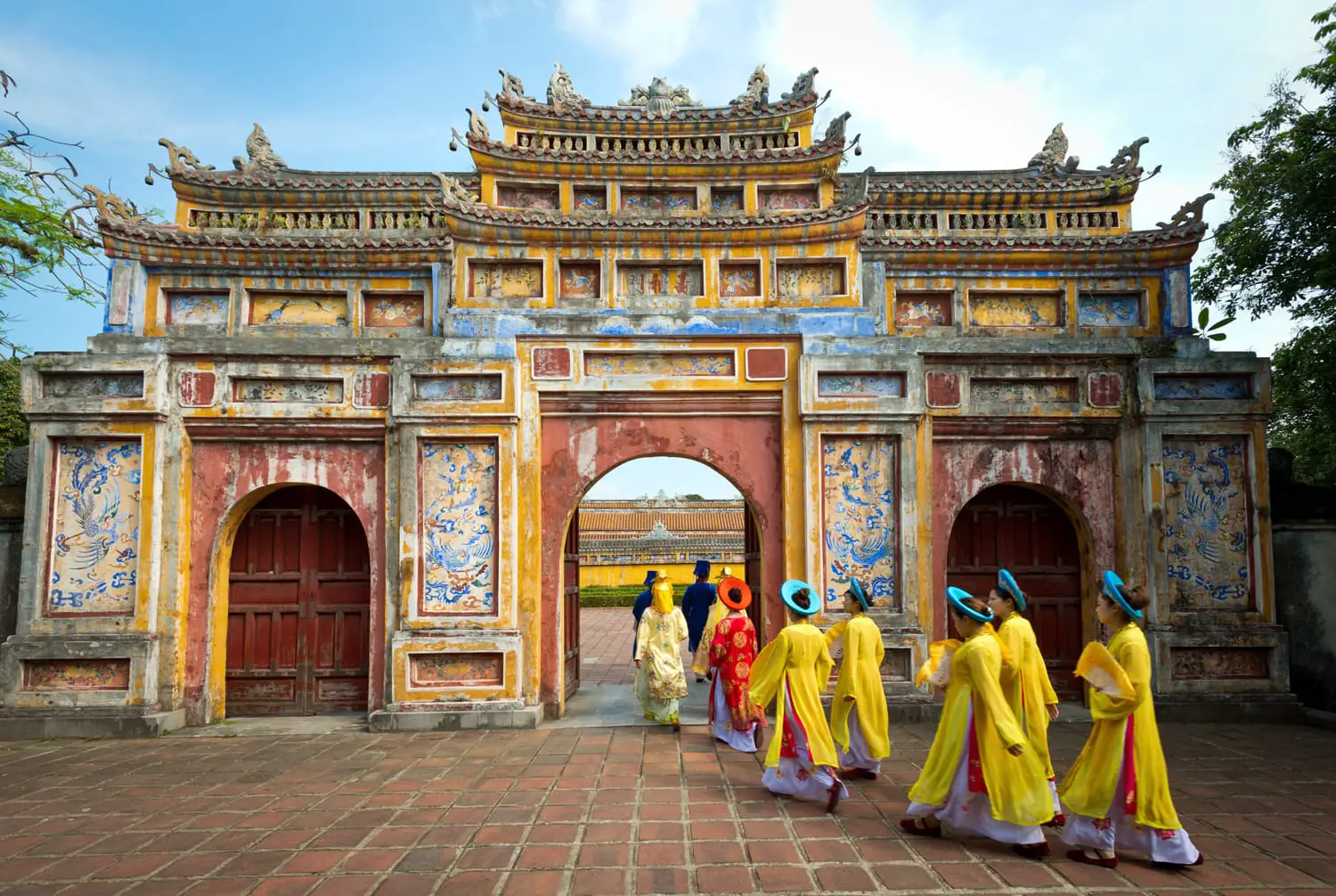 People in traditional costumes walk under an archway in the Imperial City of Hue, Vietnam.