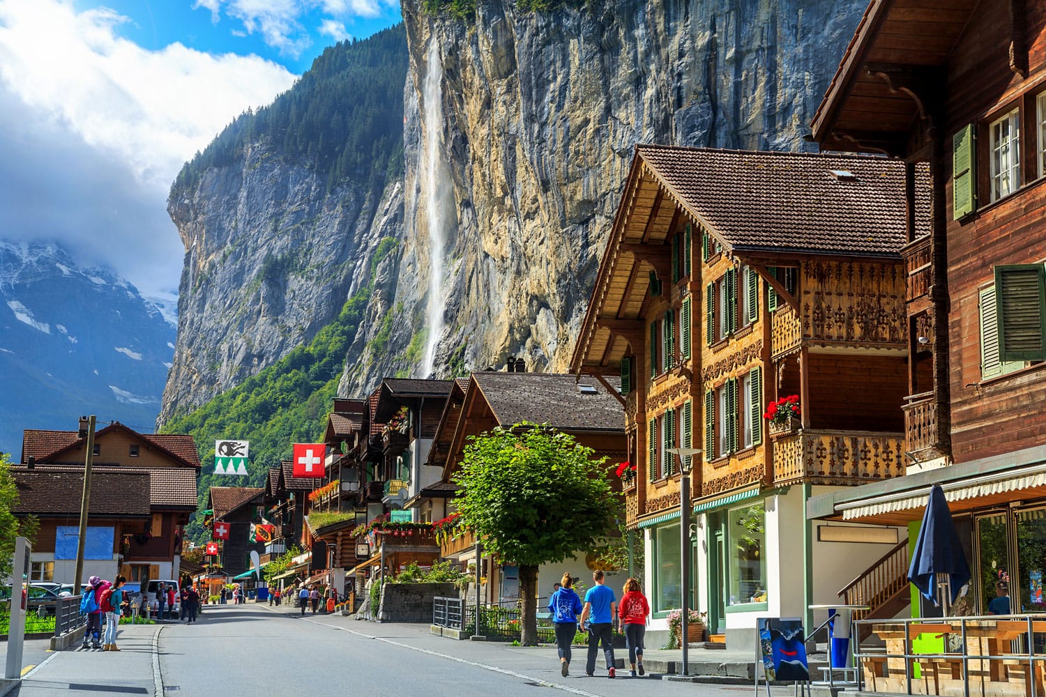 Spectacular principal street of Lauterbrunnen with shops,hotels,terraces,swiss flags and stunning Staubbach waterfall in background, Bernese Oberland, Switzerland