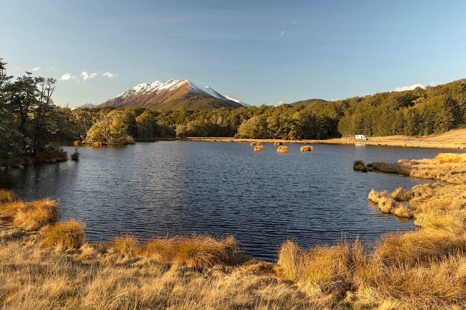 Little Mavora Lake in the south of the South Island of New Zealand with a white motorhome on the far shore with mountains in the background