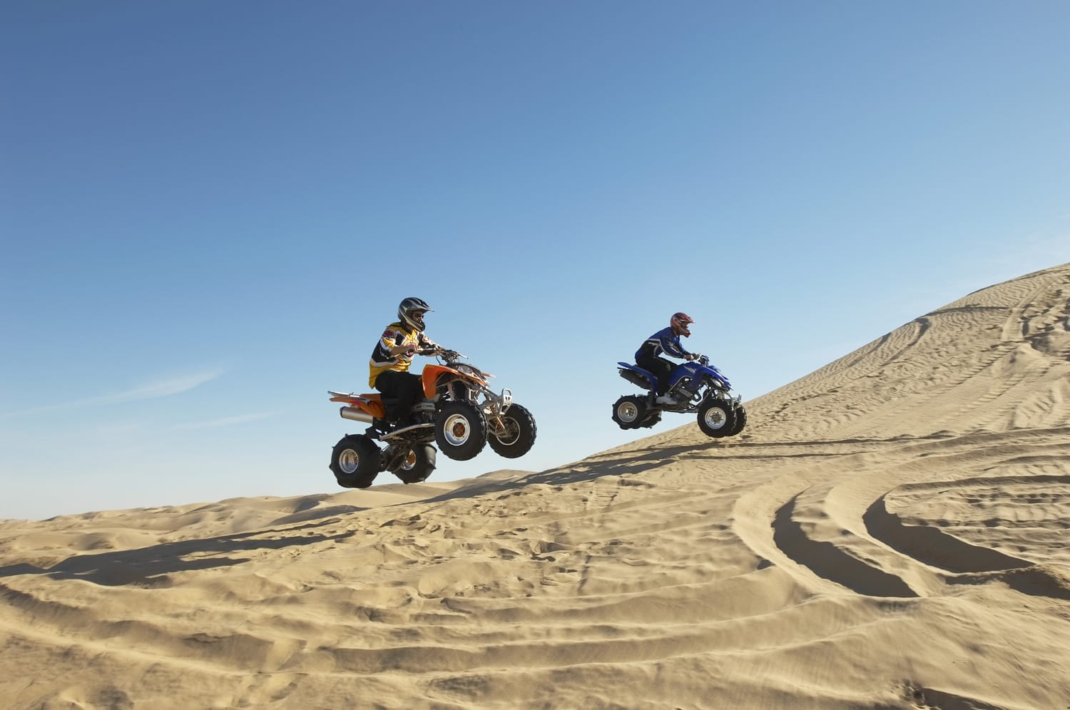 Πλάγια όψη δύο ανδρών που κάνουν wheelies με τετράποδα στην έρημο