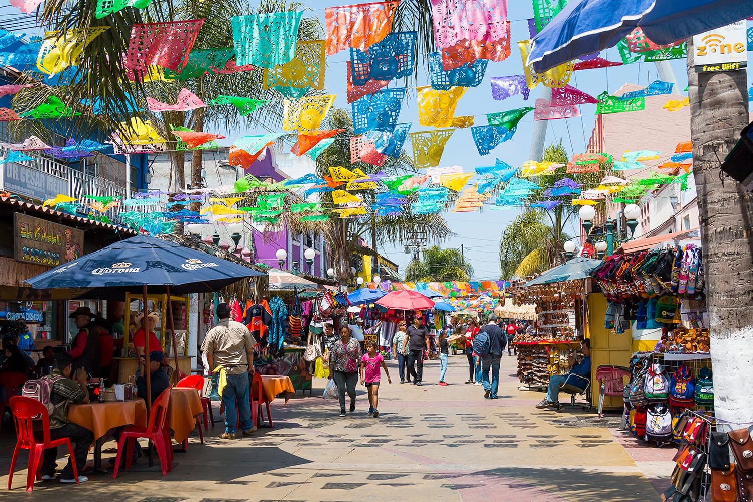 People shop and walk below colorful hanging flags at Plaza Santa Cecilia, a historic Mexican square in the heart of Tijuana, Mexico