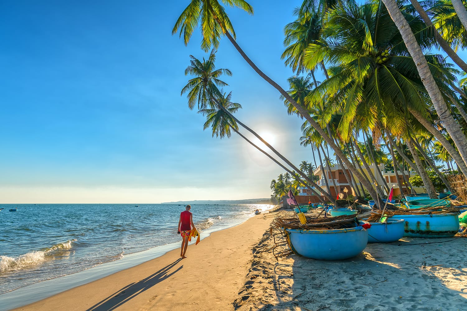 The man alone go to end of tropical beach with coconut palm trees as sun gradually create beautiful setting for weekend guests at paradise beach in Mui Ne, Vietnam