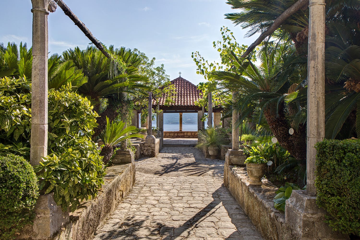 Lush vegetation, paved passageway and a pavilion at the arboretum in Trsteno, Croatia.