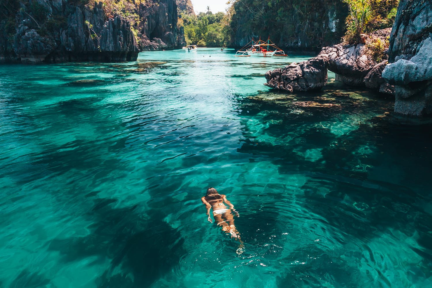 Young woman swimming in clear sea water in lagoon and looking at beautiful landscape. Travelling tour in Asia: El Nido, Palawan, Philippines