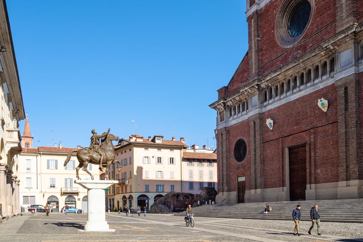 People walk near monument Regisole and Cathedral on Piazza del Duomo in Pavia, Italy