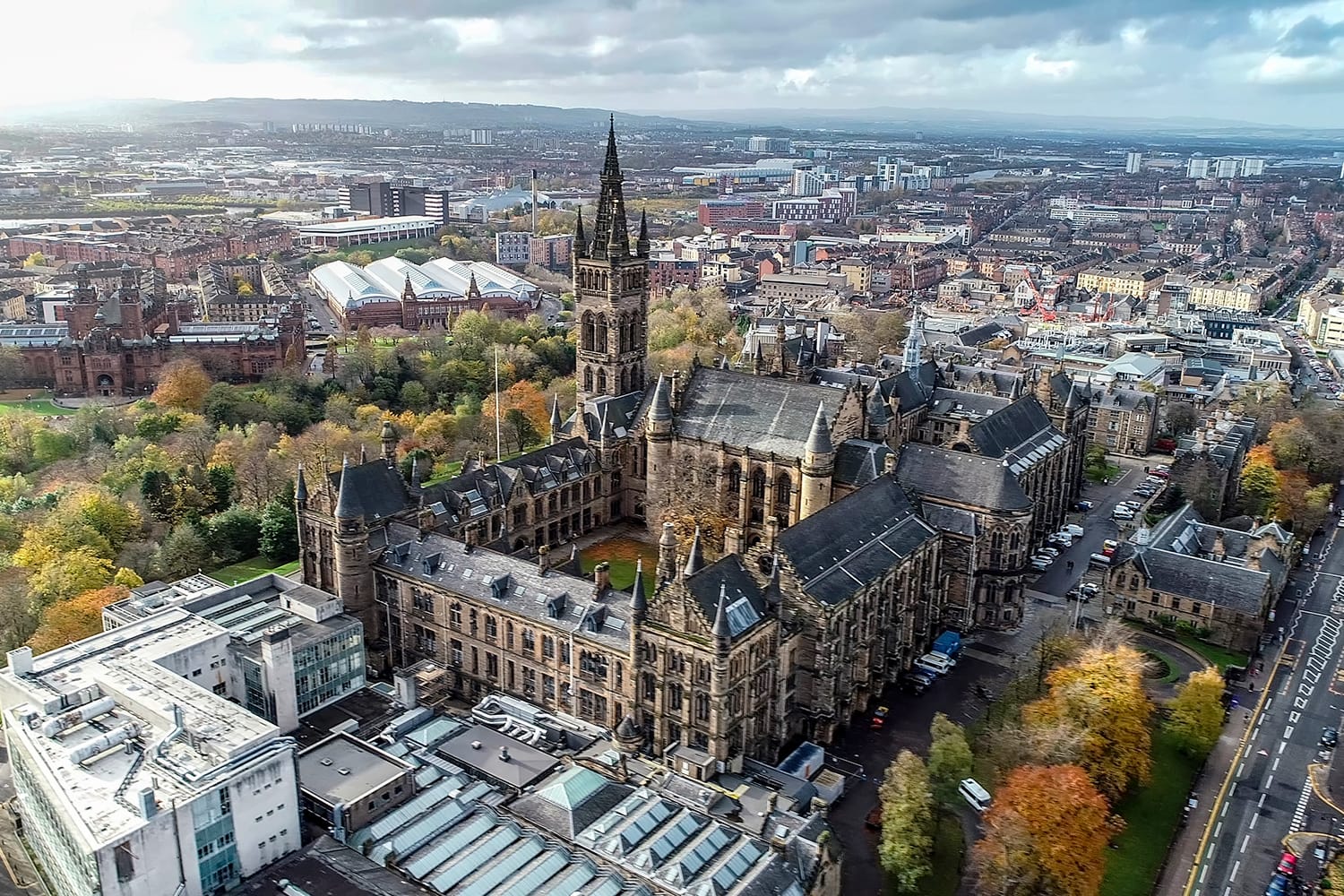 Low level aerial image over the autumn foliage of trees in Kelvingrove Park, Glasgow, to the gothic tower of Glasgow University with the cityscape behind.