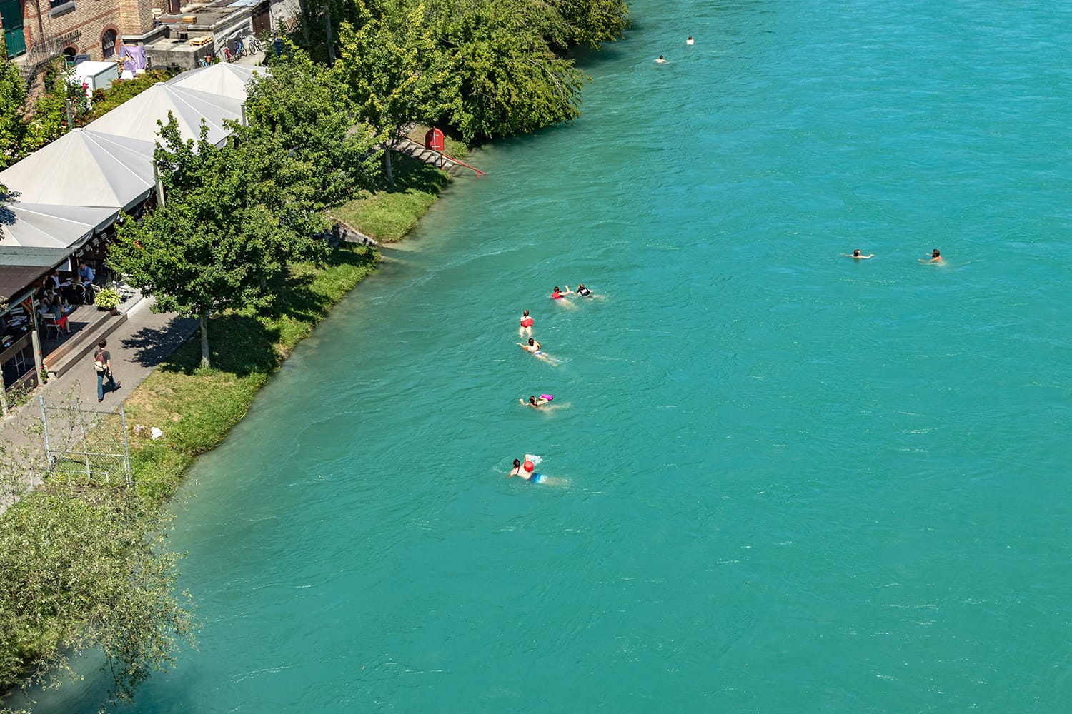 View of Aare river at sunny summer day. Local residents relax, sunbathe and rafting in inflatable boats along the fast flow of the river.