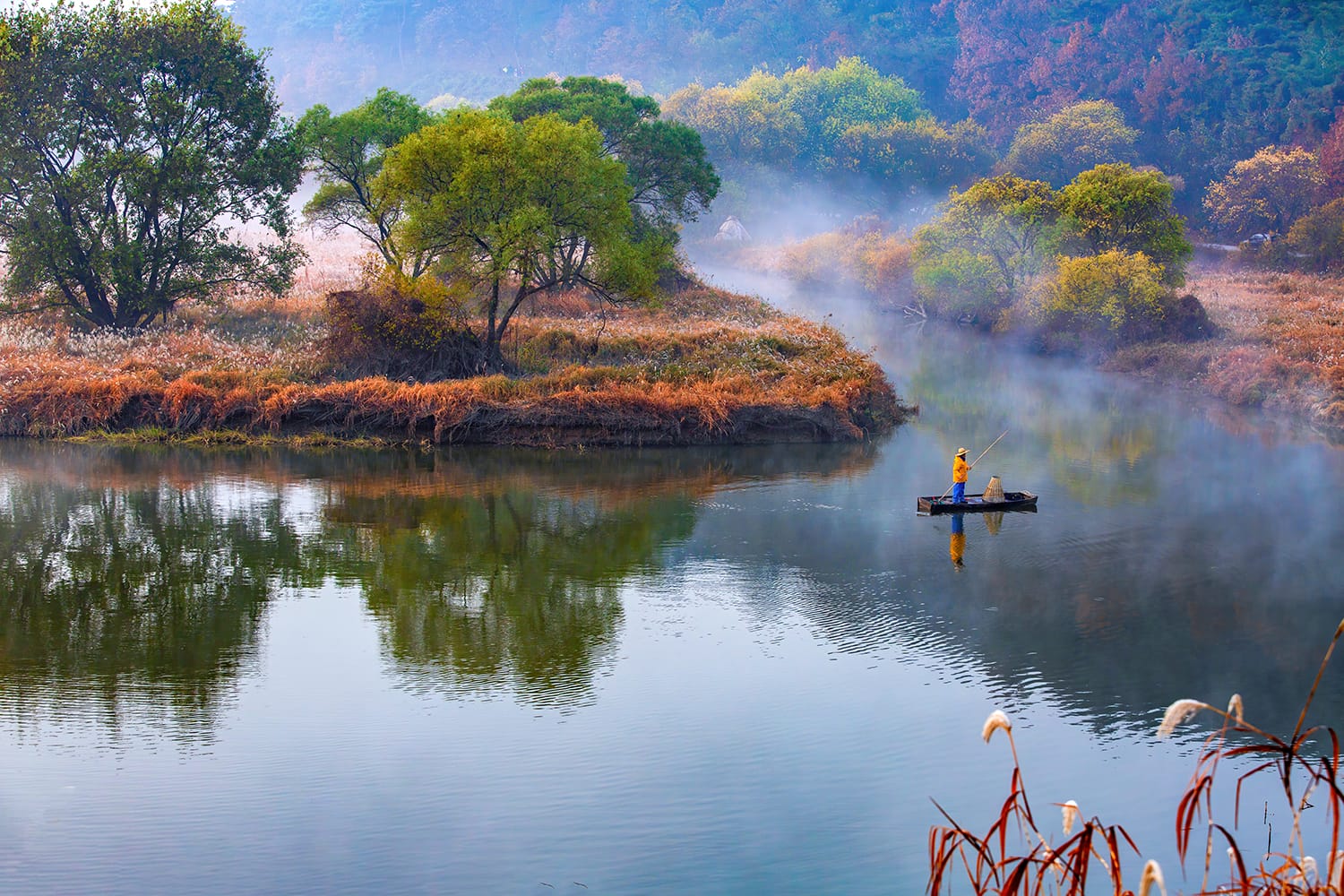 A fisherman is standing on boat with bamboo pole at foggy Upo wetland in the morning