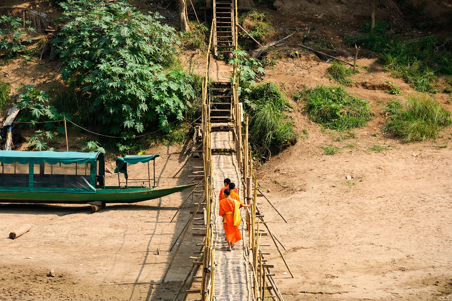 Three unidentified Buddhist monks are crossing the Bamboo Bridge that run across the Nam Khan river. The Bamboo Bridge is hand made out of bamboo and is one of the tourists attractions in Luang Prabang, Laos.