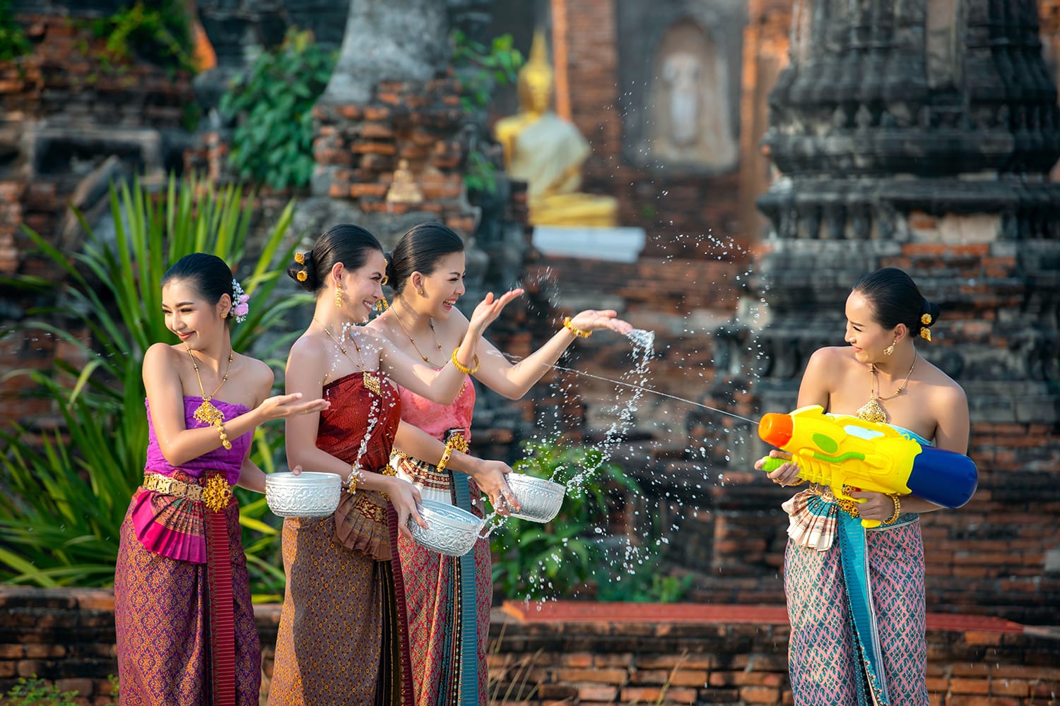 Water Songkran festival. Asia young woman wearing Thai traditional costume play water in Songkran day water festival of Thailand. Women group using water gun and bolw play in the temple.