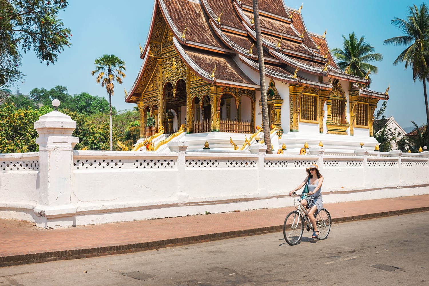 Girl tourist riding a bicycle in Luang Prabang against the backdrop of a traditional temple.A popular way among tourists is to visit Luang Prabang in Laos - a bicycle.