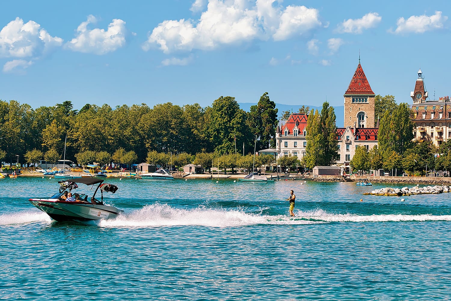 Motorboat with man wakeboarding on Lake Geneva embankment near Chateau Ouchy in Lausanne, Switzerland.