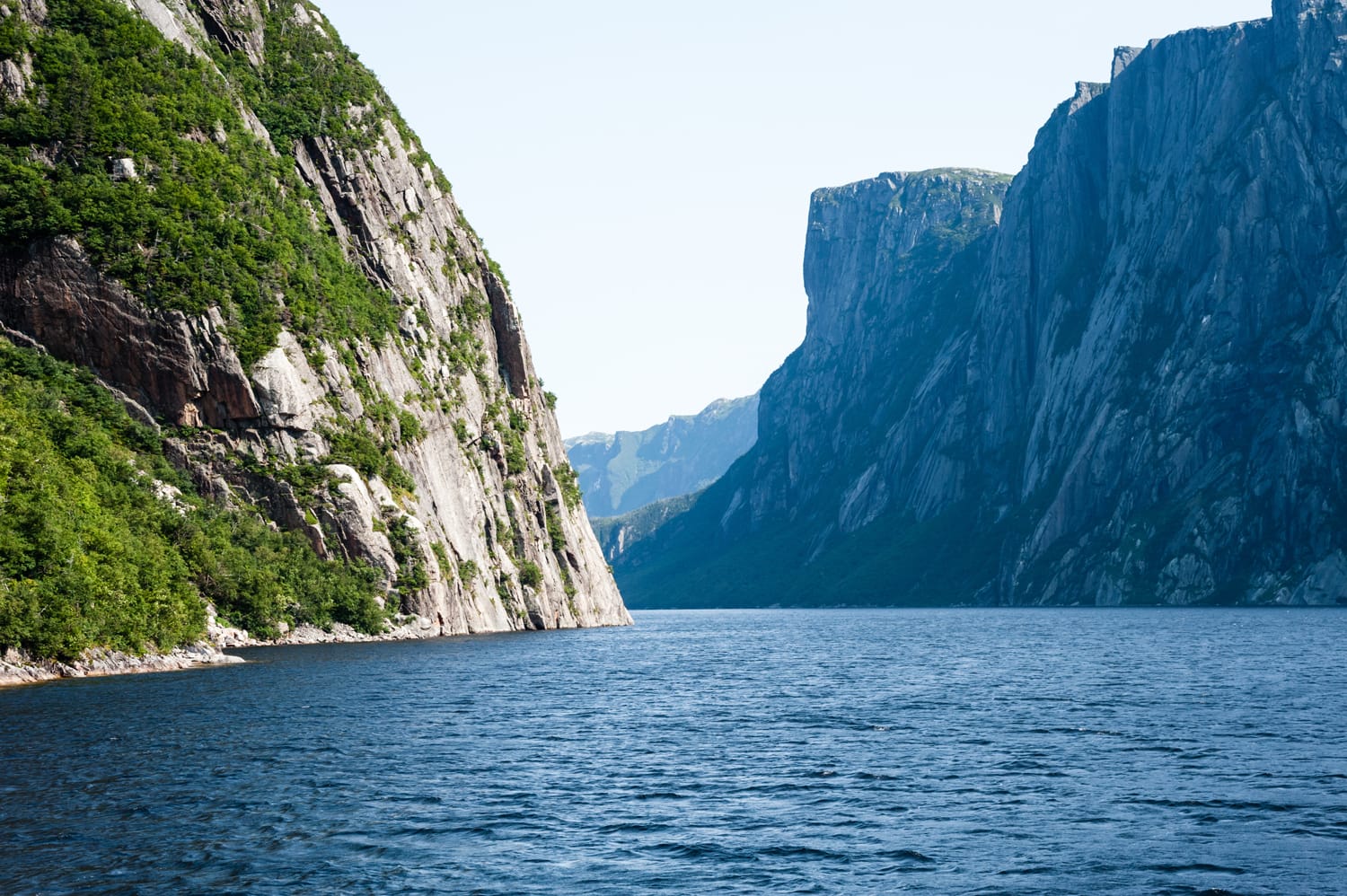 Inland fjord between large steep cliffs with some green vegetation on rock face, at Western Brook Pond, Gros Morne National Park, Newfoundland, Canada.
