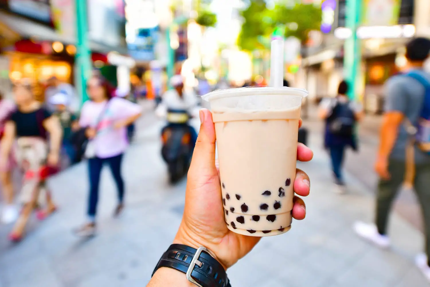 Hand holding a plastic glass of Taiwan iced bubble milk tea on crowded street background