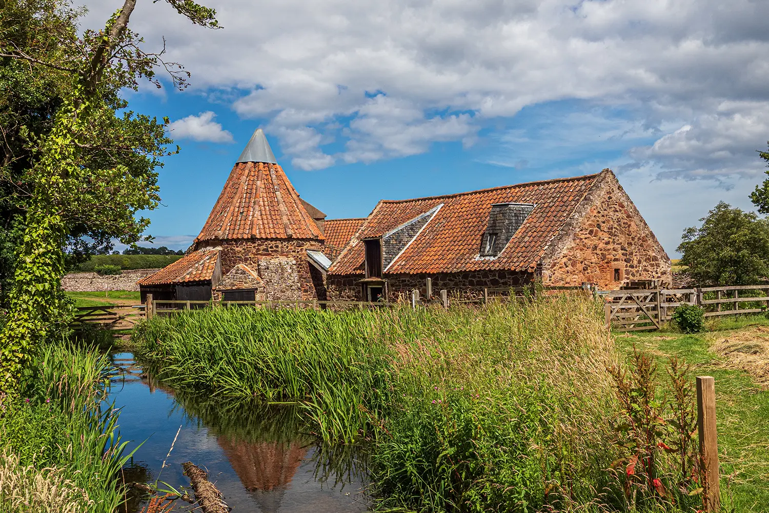 Preston Mill, East Lothian, Scotland, warm sunny day with ancient building reflected in calm water, it is also used as a film location in The Outlander series