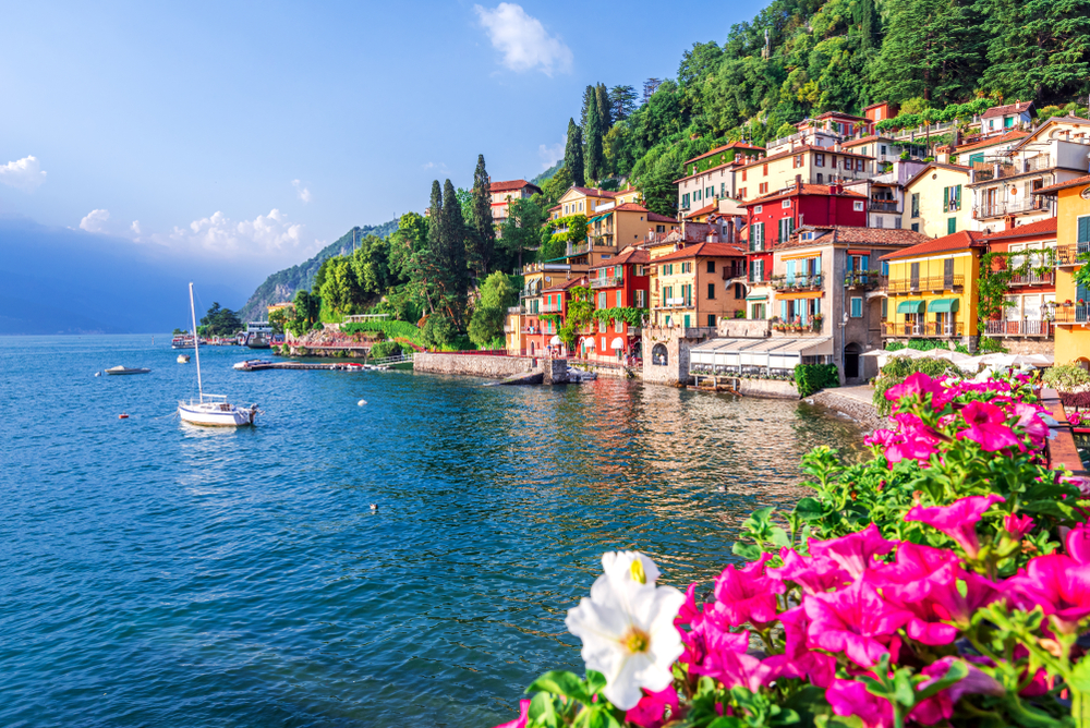 Άποψη της λίμνης Κόμο που απεικονίζεται την καλύτερη στιγμή για να επισκεφτείτε τις ιταλικές λίμνες στα τέλη της άνοιξης, με λουλούδια να ανθίζουν και βάρκες στο νερό