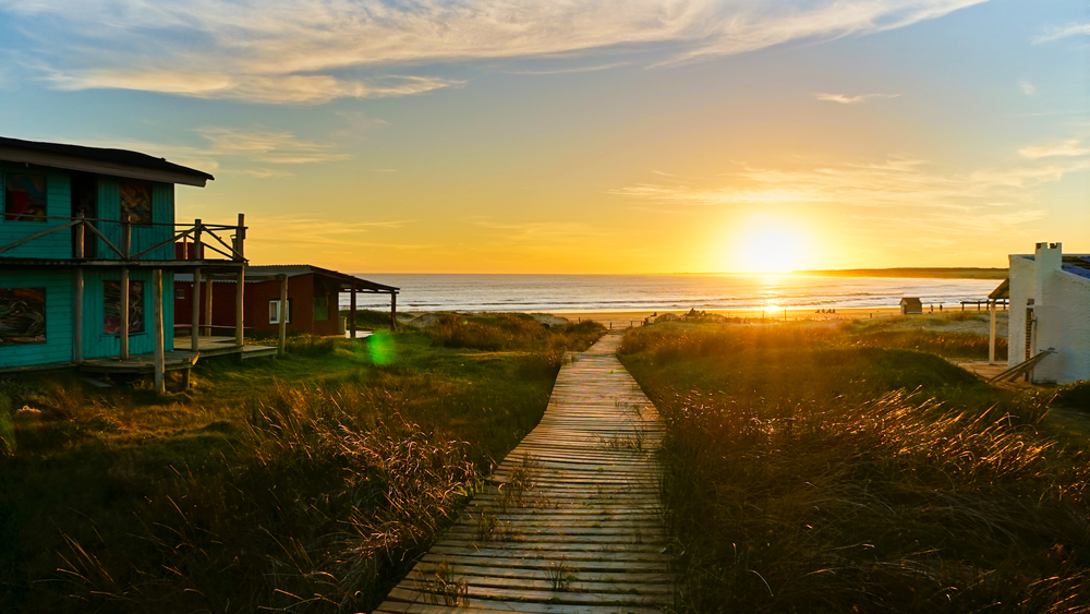 Ο ήλιος δύει πάνω από τον ωκεανό και φωτίζει τον ουρανό με μια φωτεινή πορτοκαλί λάμψη κατά τη φθηνότερη περίοδο για να επισκεφθείτε την Ουρουγουάη